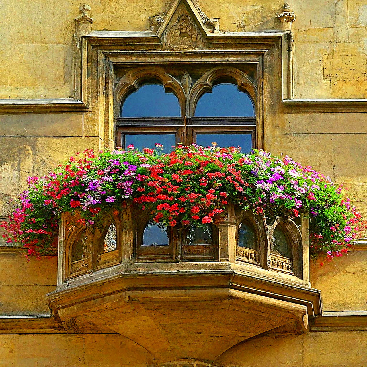 Arched balcony window with colorful flower boxes on yellow wall