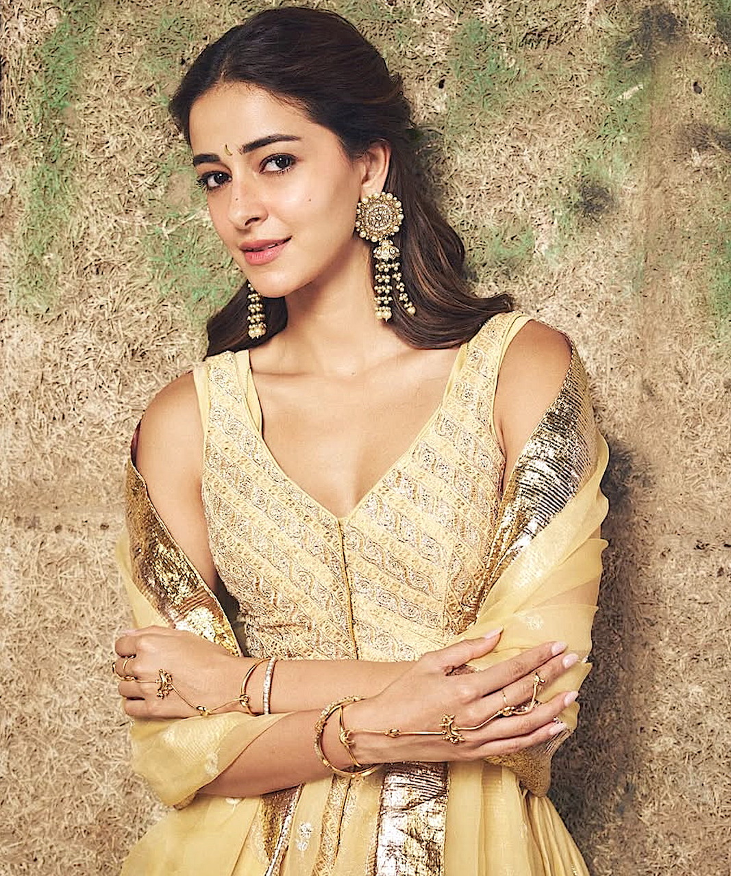 Woman in cream embroidered Indian anarkali dress with statement earrings posing against textured wall