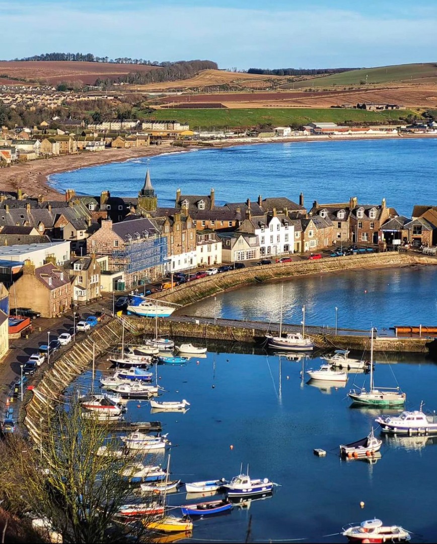 Aerial view of Stonehaven Harbour with boats, village buildings, and rolling hills