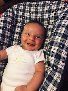Smiling baby in white onesie lying on a navy blue and white plaid fabric