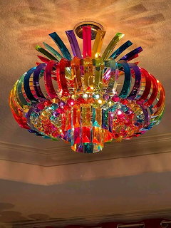 Ornate multicolored glass chandelier with curved rainbow arms and crystals on beige ceiling