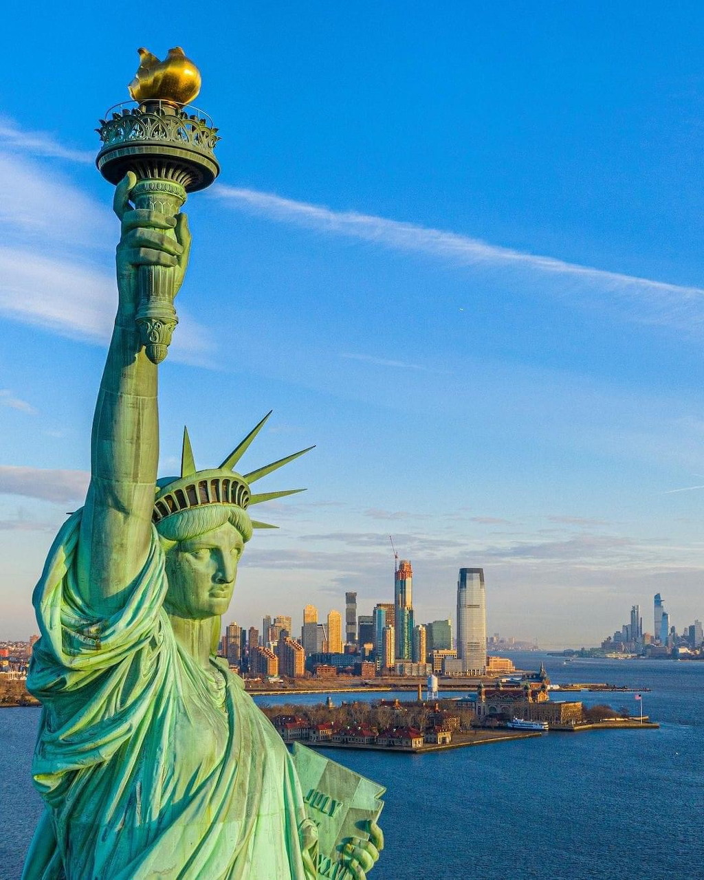 Statue of Liberty with New York City skyline in background across harbor waters