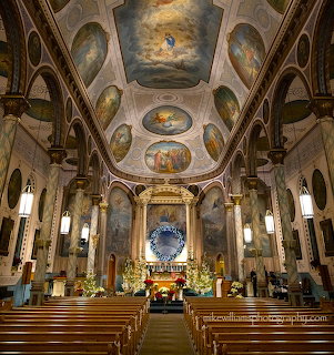 Ornate church interior with decorated ceiling, altar, pews, and warm lighting