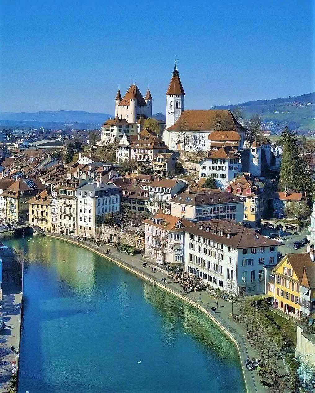 Aerial view of Swiss town with castle, river, and colorful buildings along waterfront under blue sky