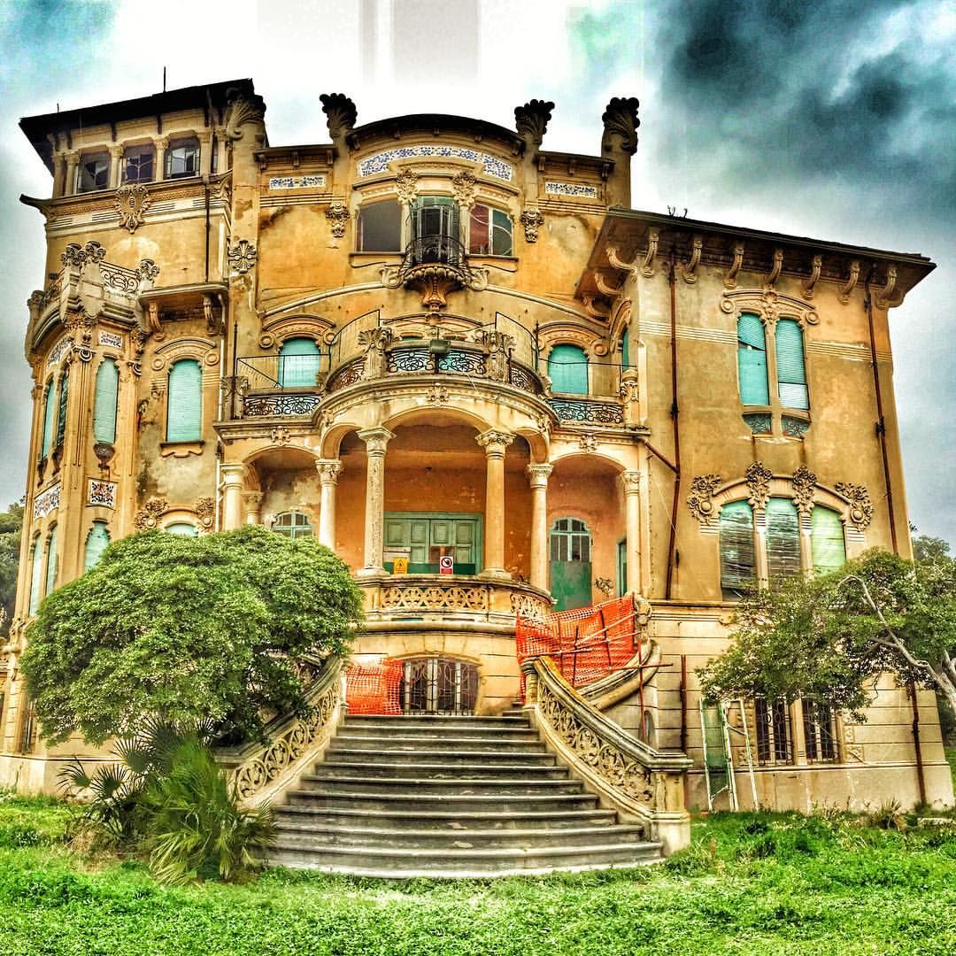 Weathered yellow Victorian villa with ornate balconies and grand staircase, surrounded by greenery