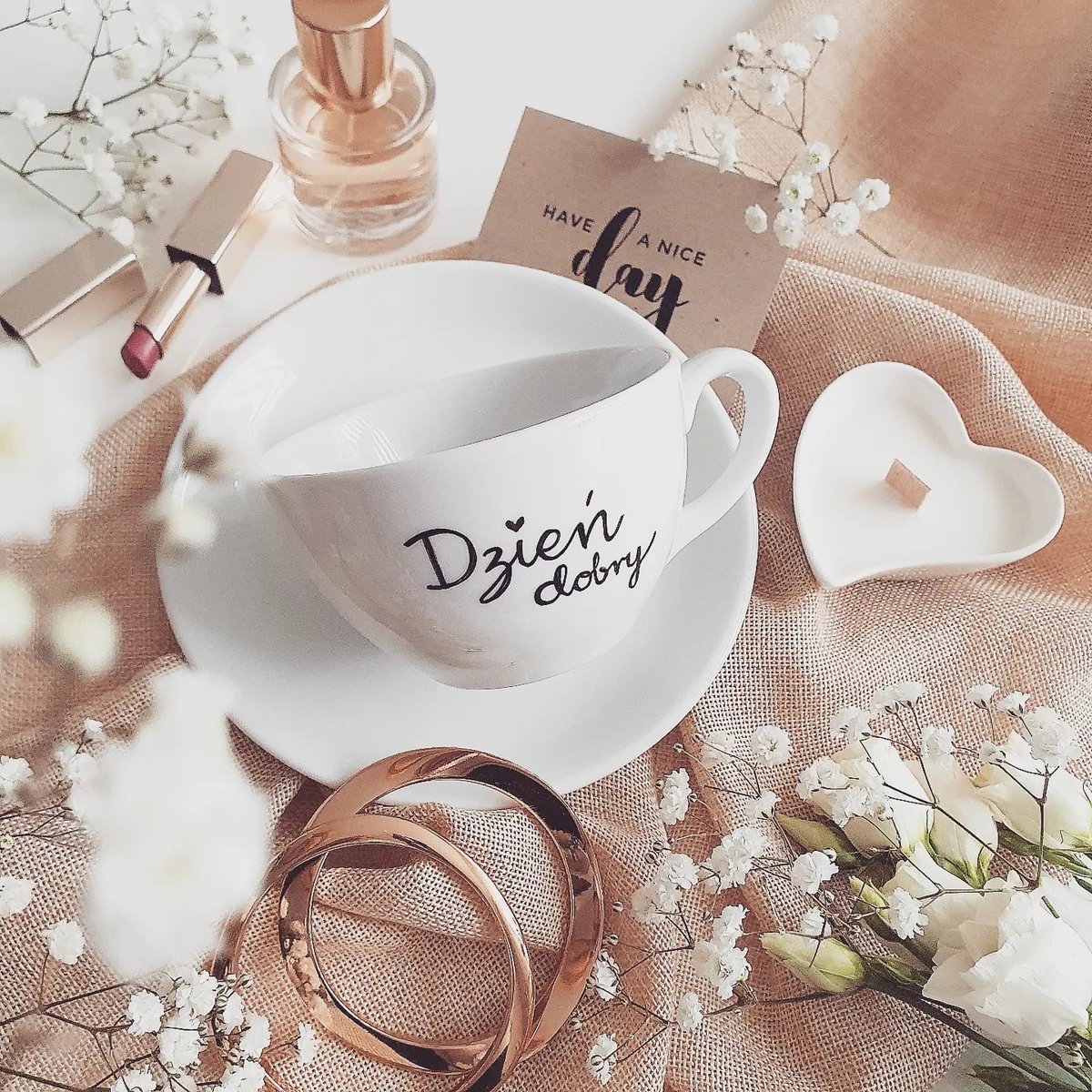 White coffee cup with Polish good morning text surrounded by flowers and decorative items on peach fabric