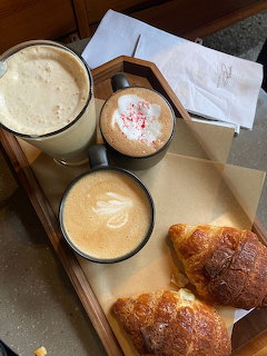 Tray with three coffee drinks, two croissants, and a napkin on a cafe table