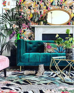 Eclectic living room with teal velvet sofa, tropical plants, colorful wallpaper, and mixed pattern decor
