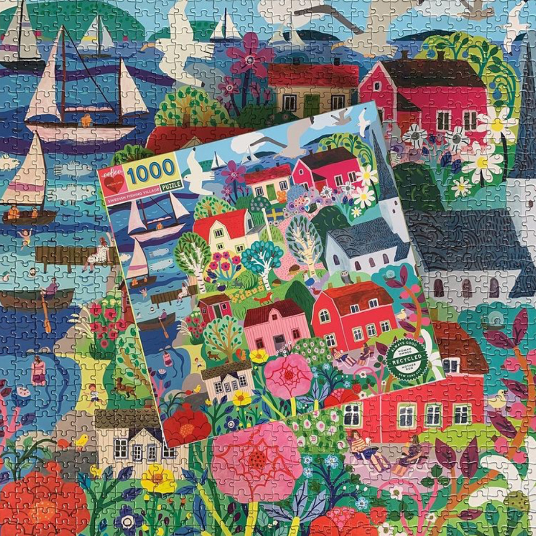 Photo of a colorful completed jigsaw puzzle and box showing houses, flowers, boats, and water