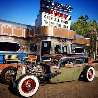 Vintage hot rod parked outside a retro diner with a tall sign