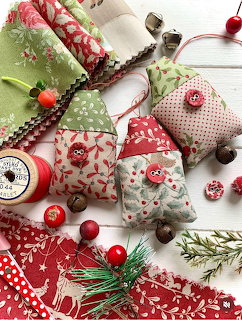 Handmade Christmas fabric ornaments with red and green patterns, buttons, thread spools, and pine on white wood
