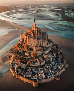 Aerial view of Mont Saint-Michel island monastery surrounded by tidal sand flats at sunset