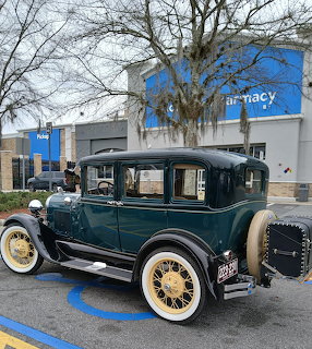 Dark green 1929 Ford Model A sedan with white-wall tires parked in a shopping center lot