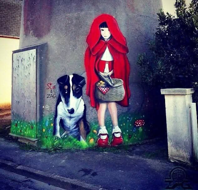 Street art mural of a red-hooded girl beside a black and white dog near a gravestone