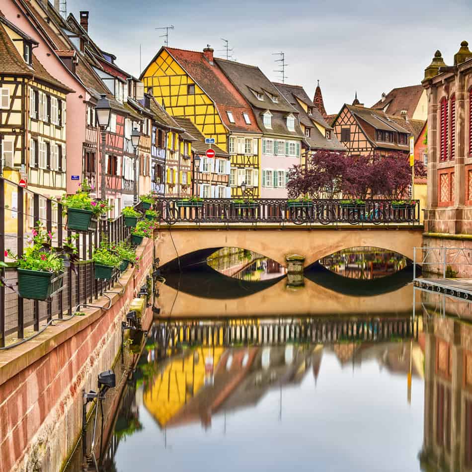 Colorful half-timbered buildings and a stone bridge reflected in a canal in Colmar, France