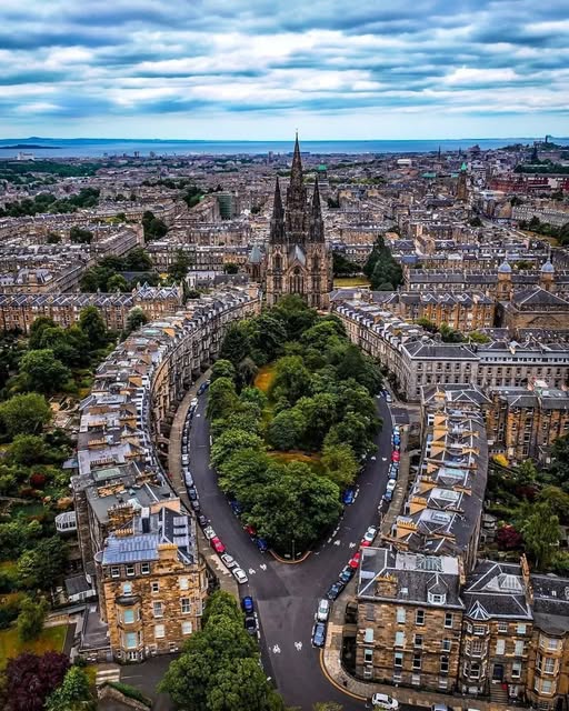 Aerial view of Edinburgh cityscape with Gothic church spire, historic stone buildings, and green trees