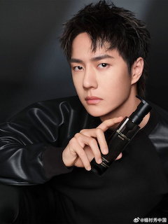 Young Asian man in black outfit holding a luxury cosmetic product in a studio portrait