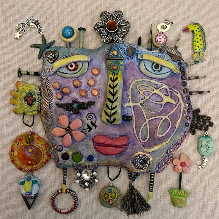 Colorful mixed media naive art face assemblage with flowers, charms, and decorative found objects
