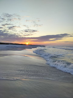Waves washing onto a sandy beach at sunset under a cloudy pastel sky
