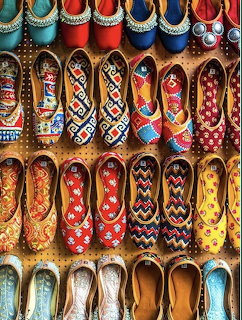 Colorful embroidered slippers with geometric patterns arranged in rows on wooden shelves