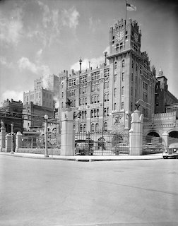 Black-and-white view of a historic brewery-style building and fenced street corner