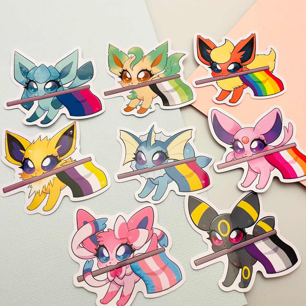 Nine Pokemon Eeveelution character stickers with various LGBTQ pride flag colors arranged on a light background