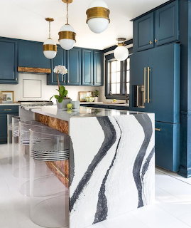 Modern kitchen with navy blue cabinets, white marble island with dramatic black veining, and gold pendant lights
