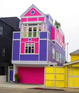 Colorful Victorian house painted in bright pink, purple and yellow with decorative trim and matching garage doors