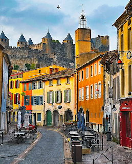 Medieval fortress towers above colorful French village street with yellow and orange buildings in Carcassonne