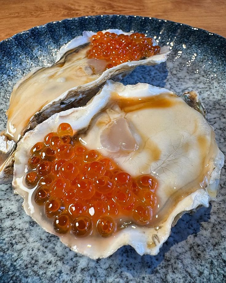Two raw oysters topped with bright orange salmon roe on a blue ceramic plate