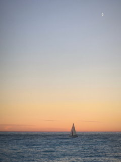 Sailboat on calm sea at sunset under a crescent moon