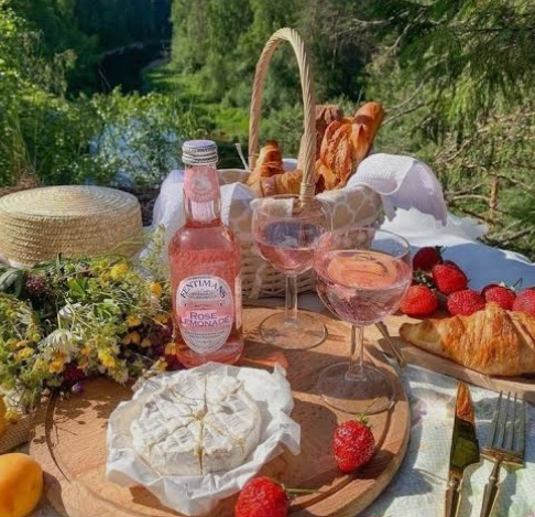 Picnic table with cheese, bread, strawberries, drinks and pastries outdoors
