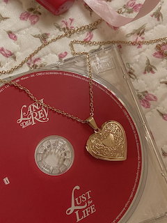 Red Lana Del Rey Lust for Life CD with gold heart locket necklace on floral fabric