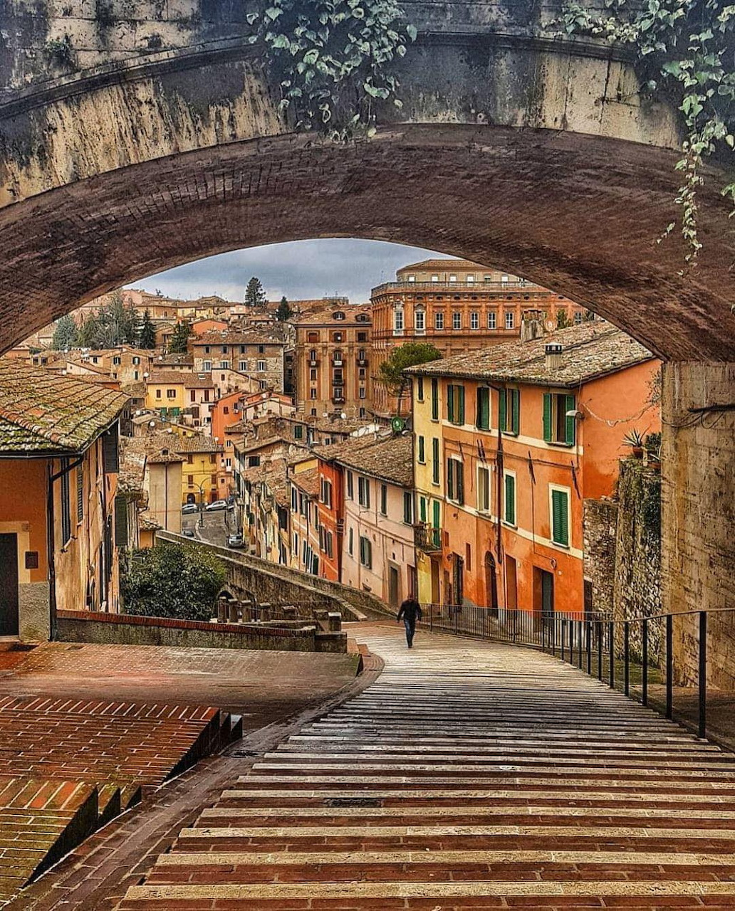 View through stone arch of colorful buildings along a stepped street in Perugia, Italy