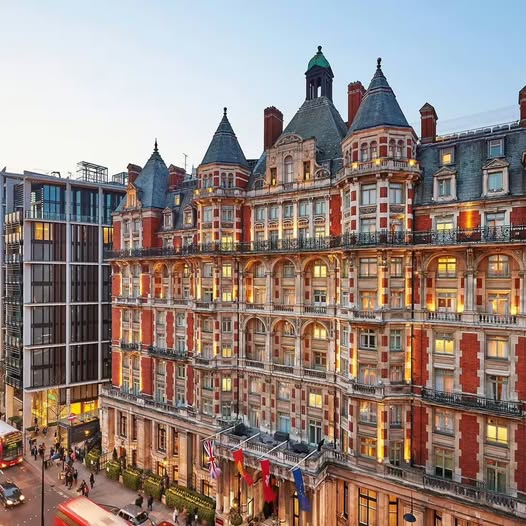 Ornate historic hotel building with glowing windows on a London street at dusk