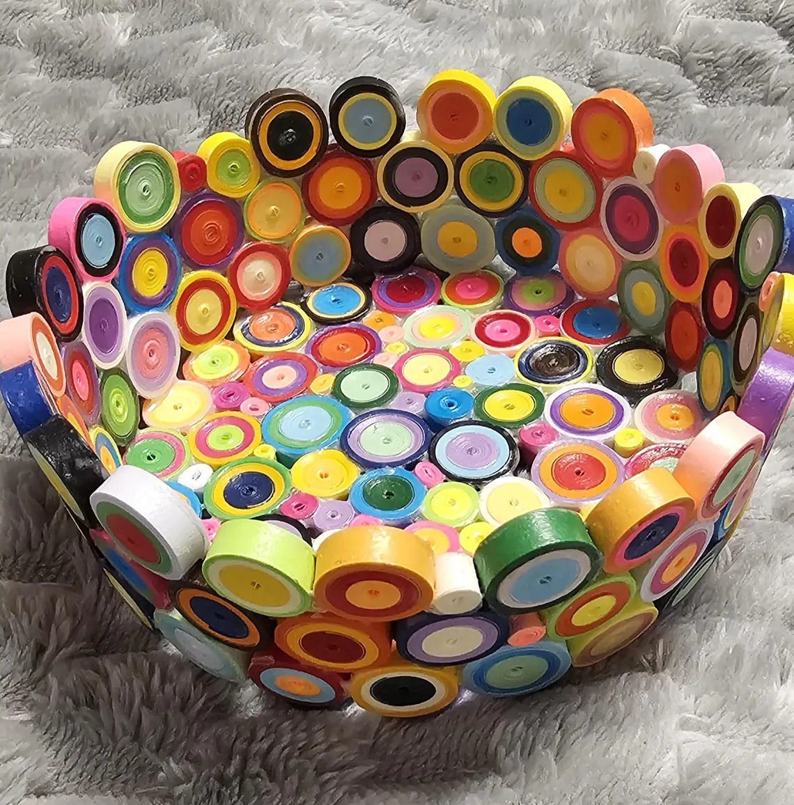 Colorful decorative bowl covered in quilled paper circles on a gray textured background