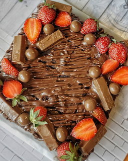 Overhead view of chocolate cake decorated with strawberries, chocolate candies, and wafer rolls with chocolate drizzle
