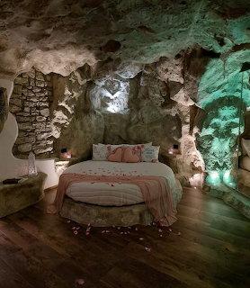 Bedroom inside a rocky cave with a bed, wooden floor, and soft green and warm lighting