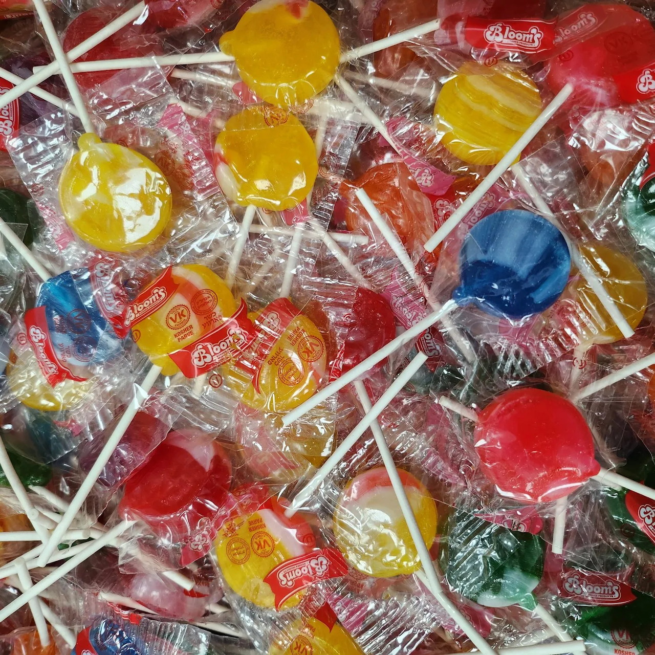 Overhead view of many wrapped lollipops in various bright colors with white sticks