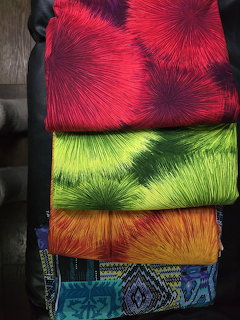 Stack of colorful vintage fabrics with starburst patterns in red, green, yellow, and orange