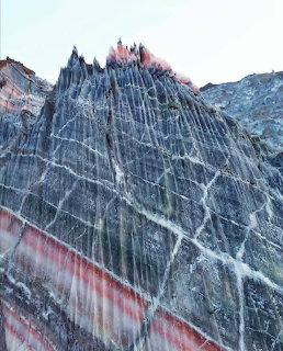 Jagged mountain peak with striking striped rock layers in gray, white and red tones