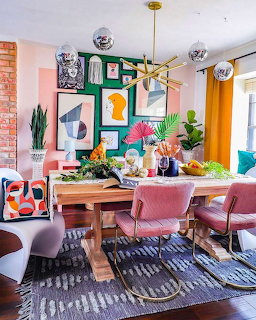 Colorful dining room with pink chairs, art gallery wall, wooden table, patterned rug, and orange curtains