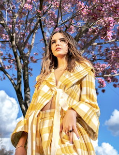 Woman in a yellow plaid coat standing under pink blossoms and blue sky