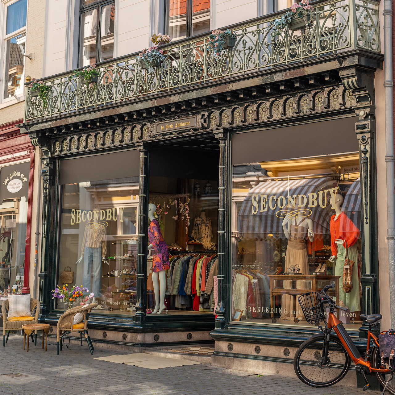 Ornate vintage storefront with large display windows and decorative balcony showing secondhand clothing shop