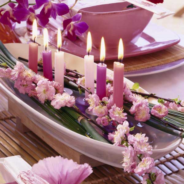 Pink candles and flowers arranged in a white bowl on a table