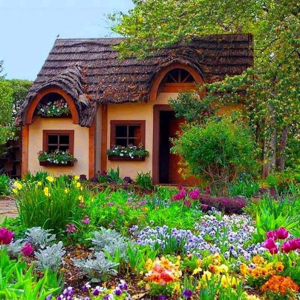 Charming thatched cottage with arched windows surrounded by colorful flower garden
