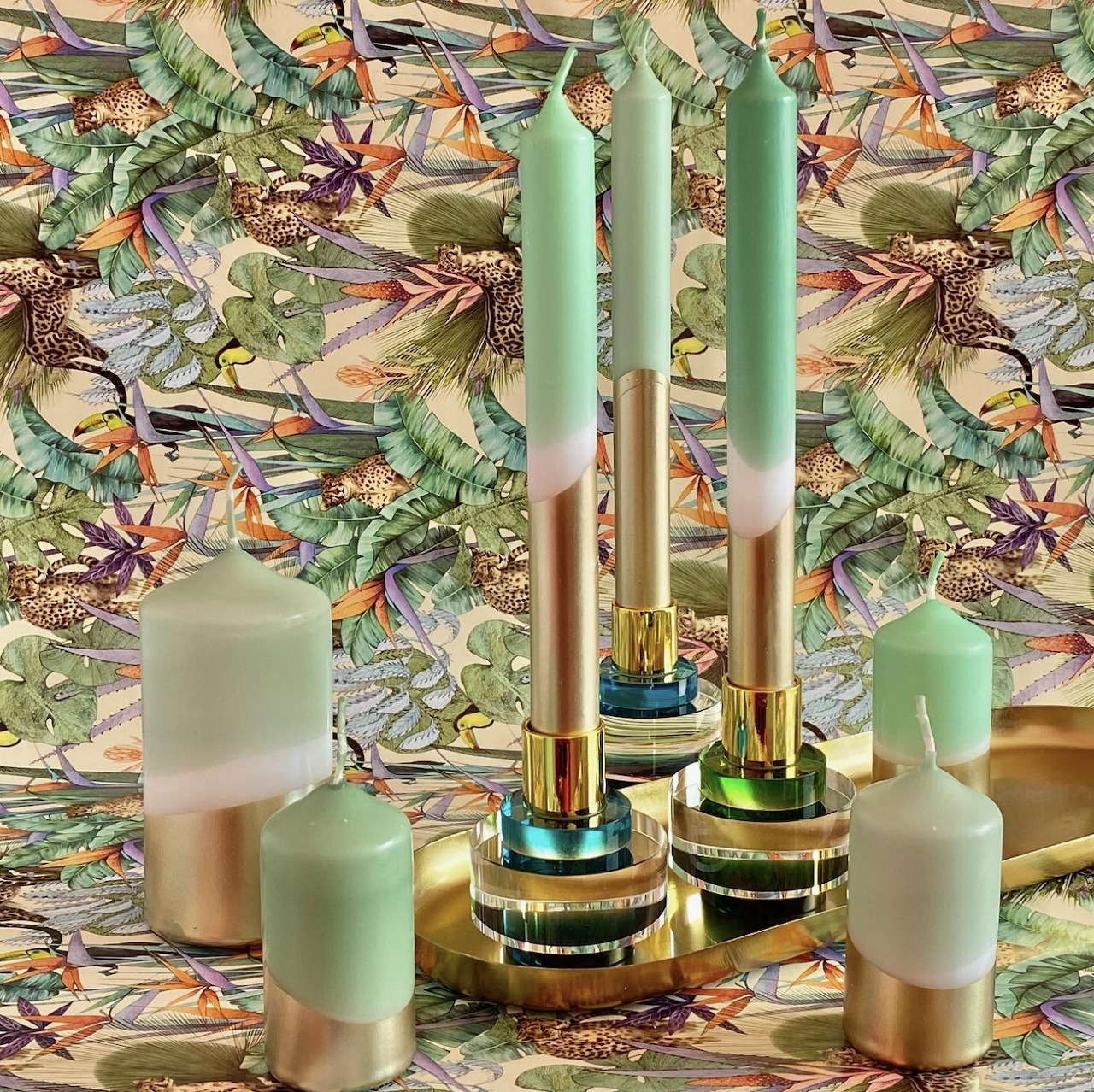 Mint green candles in gold holders against a colorful botanical patterned background