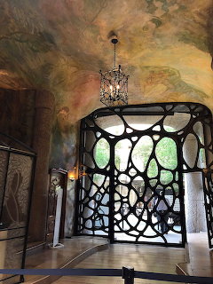 Art Nouveau interior with curved black ironwork gate, chandelier, and painted vaulted ceiling in Casa Milà