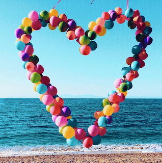 Colorful balloon heart on a beach with ocean and blue sky