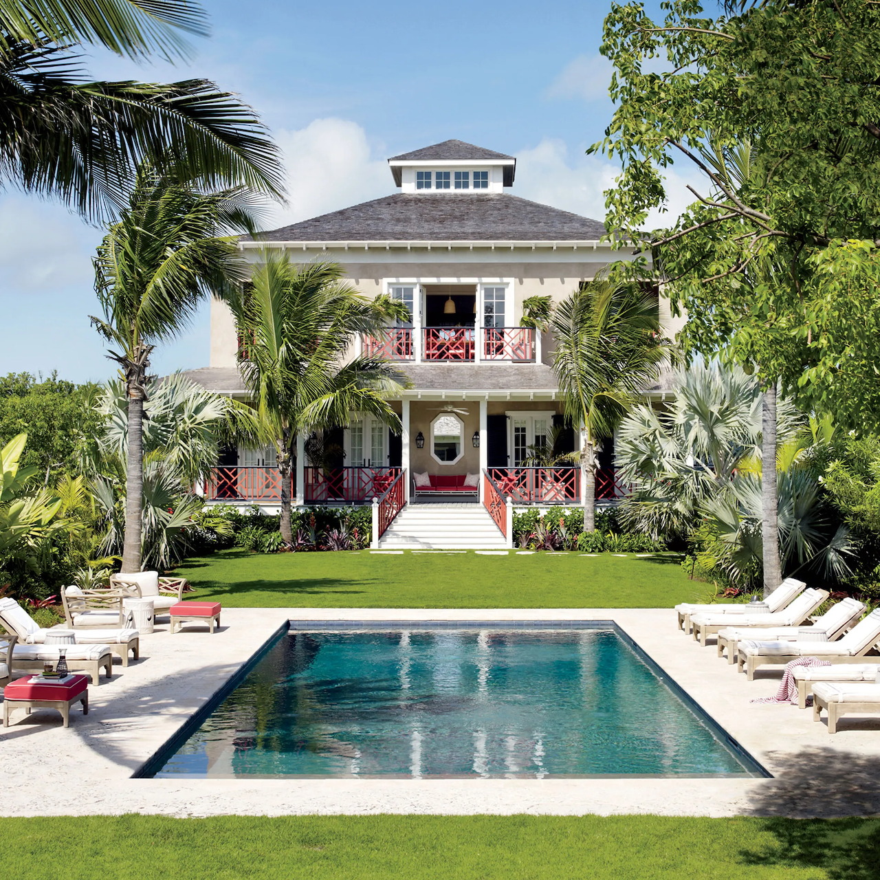 Tropical colonial-style beach house with pool, palm trees, and lounge chairs on green lawn